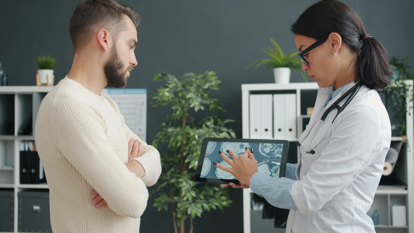 Doctor explaining a hip or joint scan on a tablet to a mature patient during a calm consultation for hip pain and mobility limits — no surgery shown