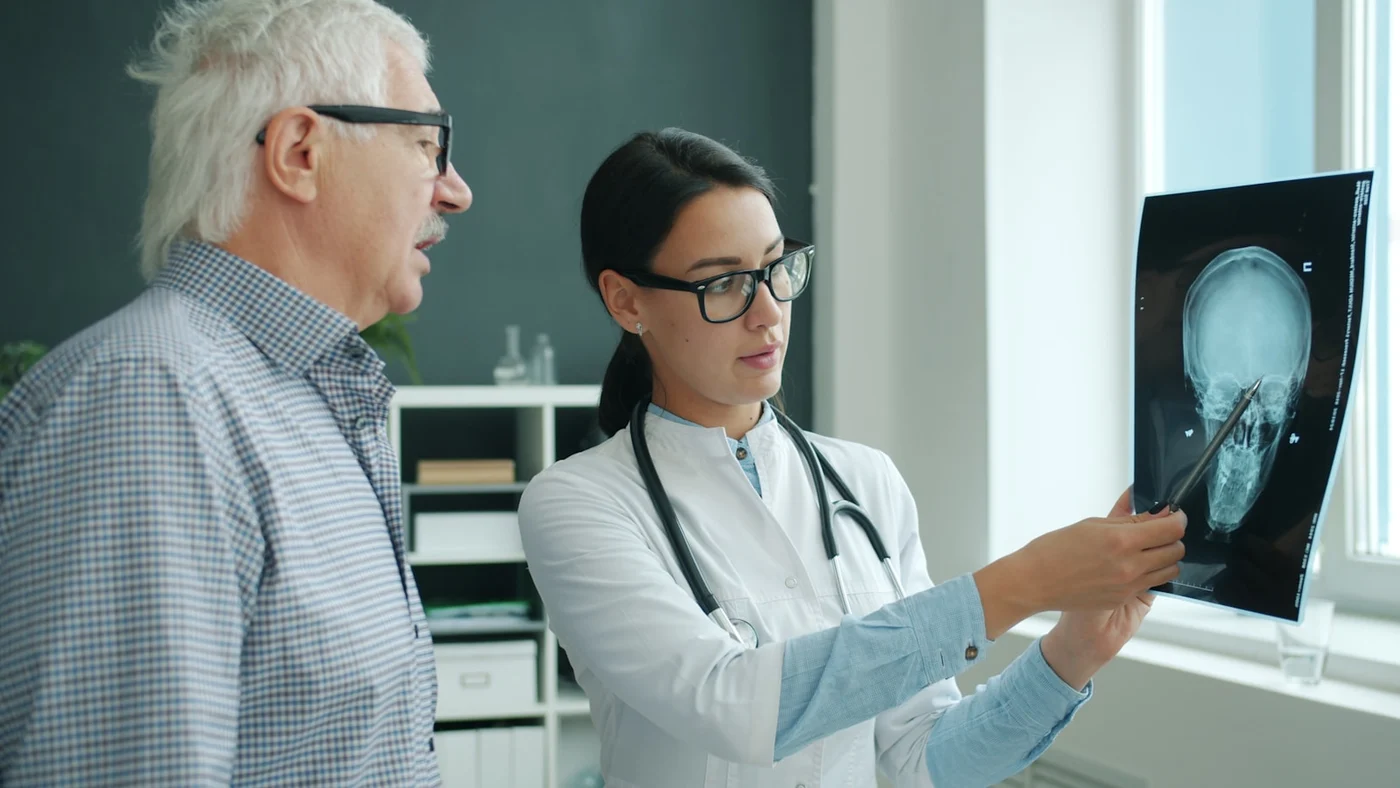 Doctor explaining a knee X-ray to a mature male patient during a calm orthopedic consultation for knee pain and walking difficulty — no surgery shown