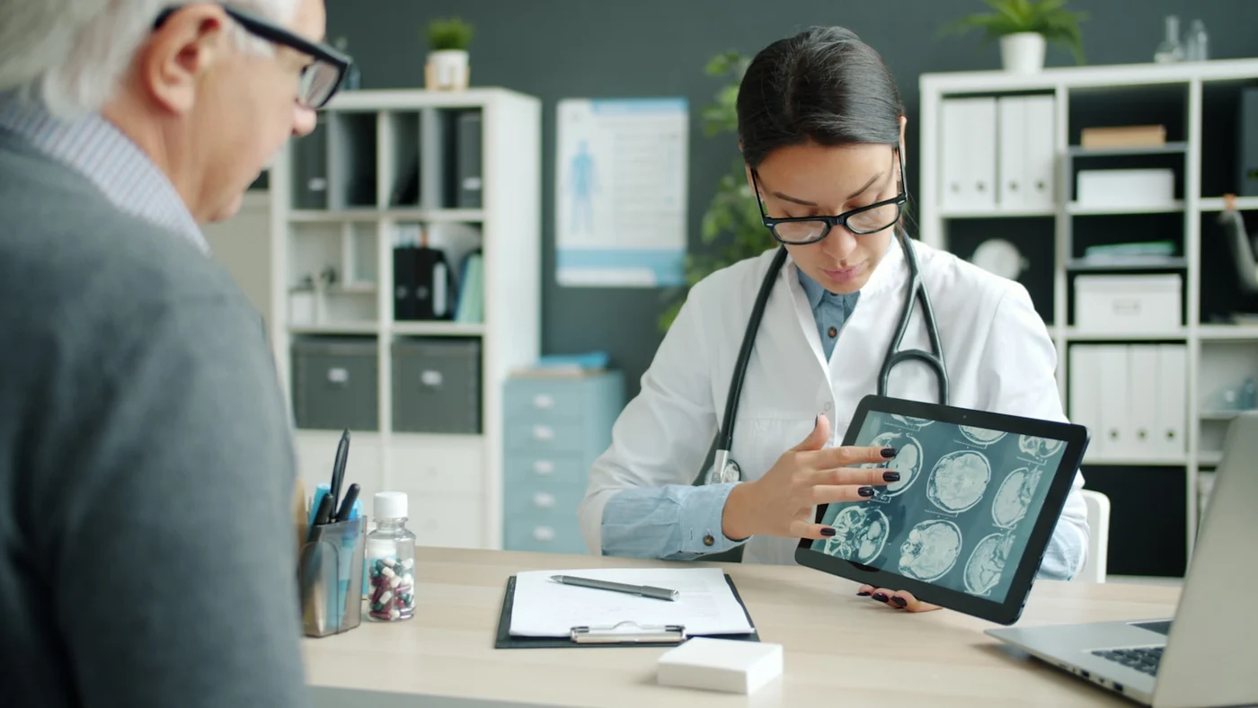 Doctor explaining joint imaging and treatment options on a tablet to a mature patient during a calm specialist review for joint replacement options — no surgery shown
